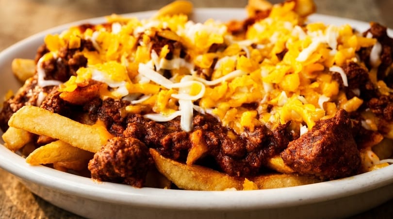 Close-up of golden french fries topped with savory chili and melted cheddar and mozzarella cheeses.