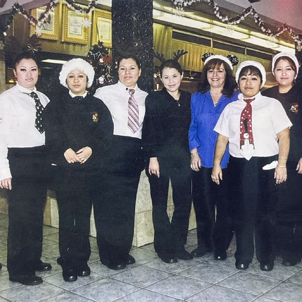 Eight female restaurant staff members in uniform and festive hats pose for a group photo.