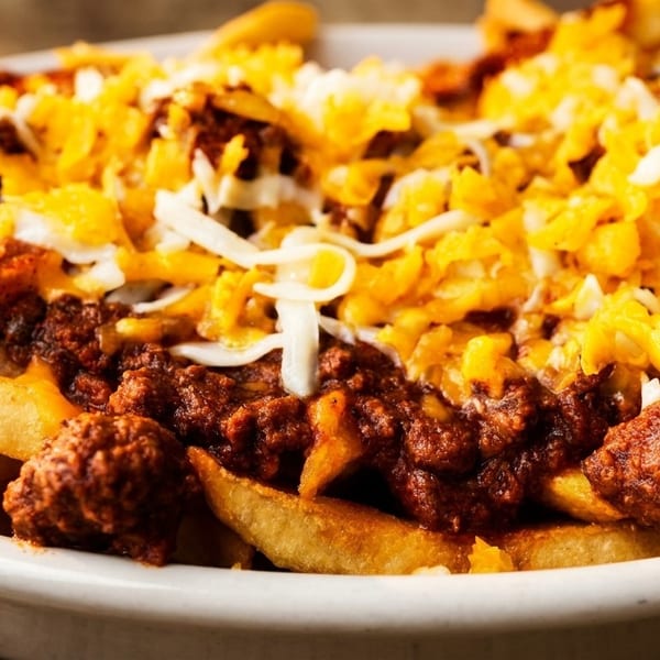 Close-up of golden french fries smothered in chili and topped with shredded cheddar and Monterey Jack cheese.