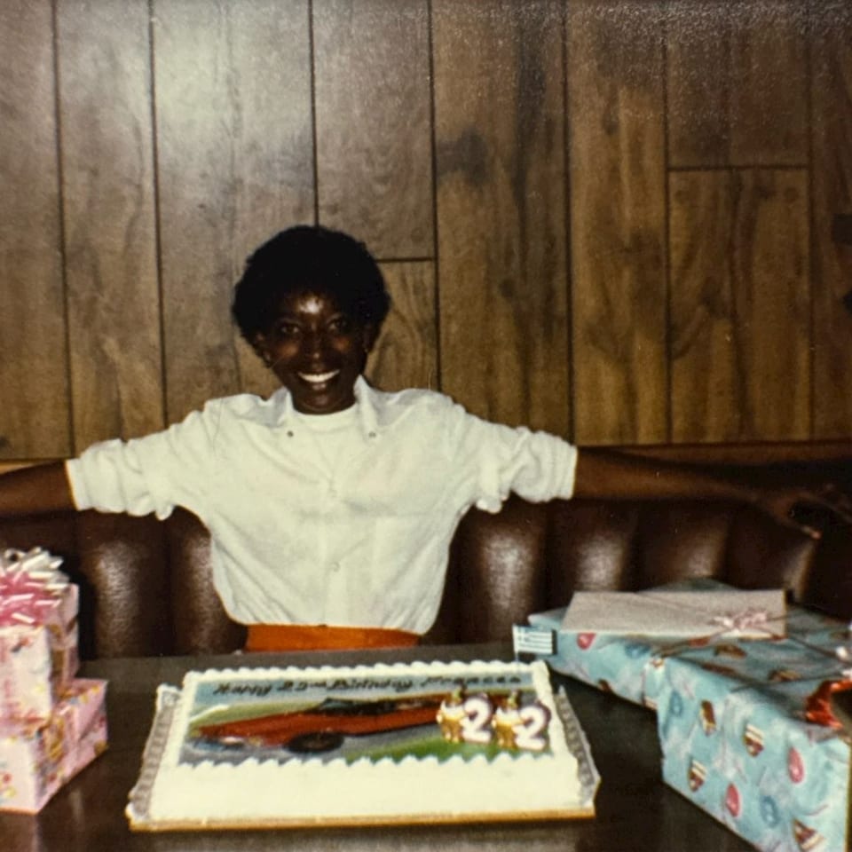 Smiling person celebrating a 22nd birthday with cake and presents at a restaurant booth.